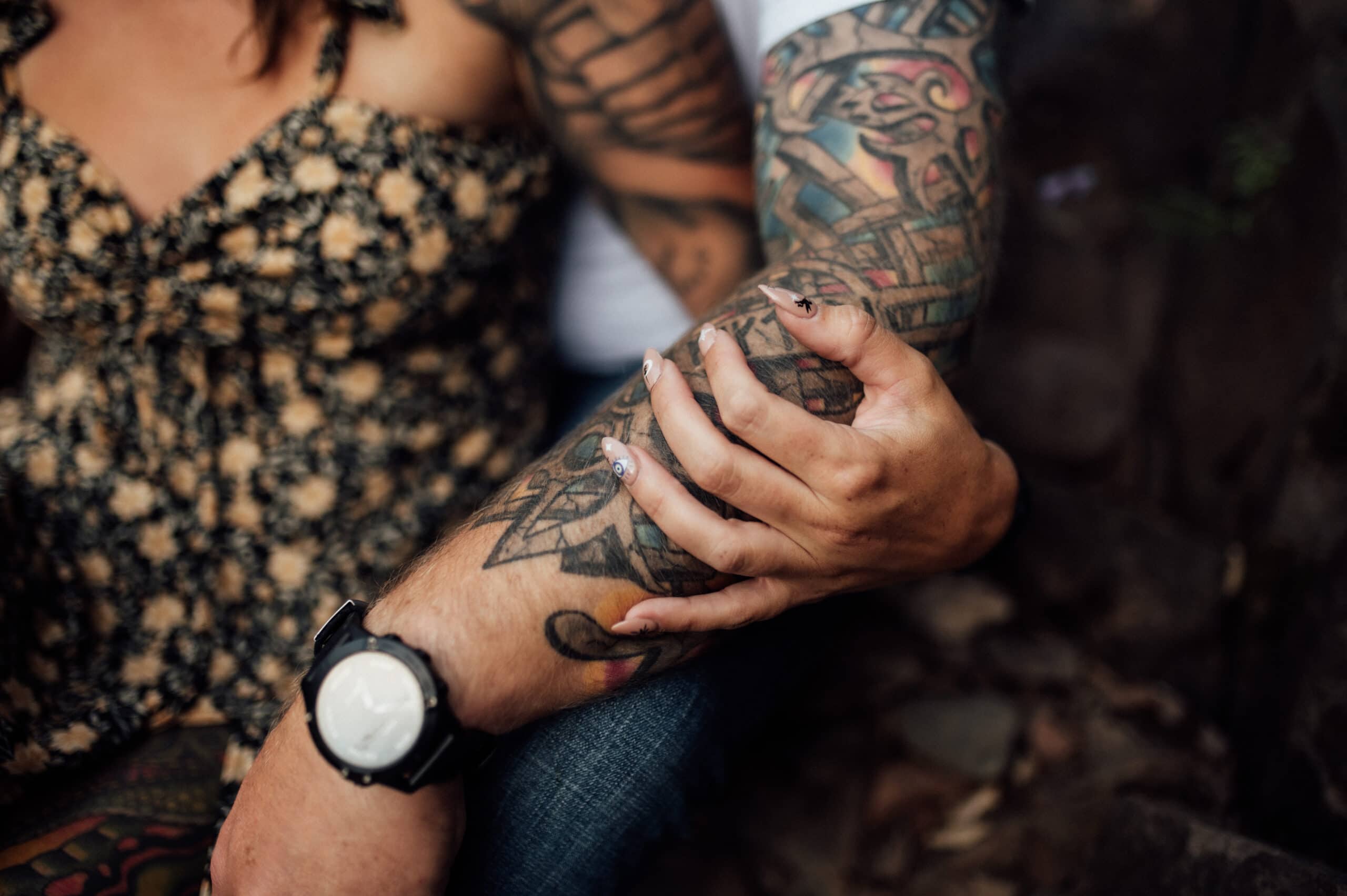 Woman's hand holding man's tattooed arm